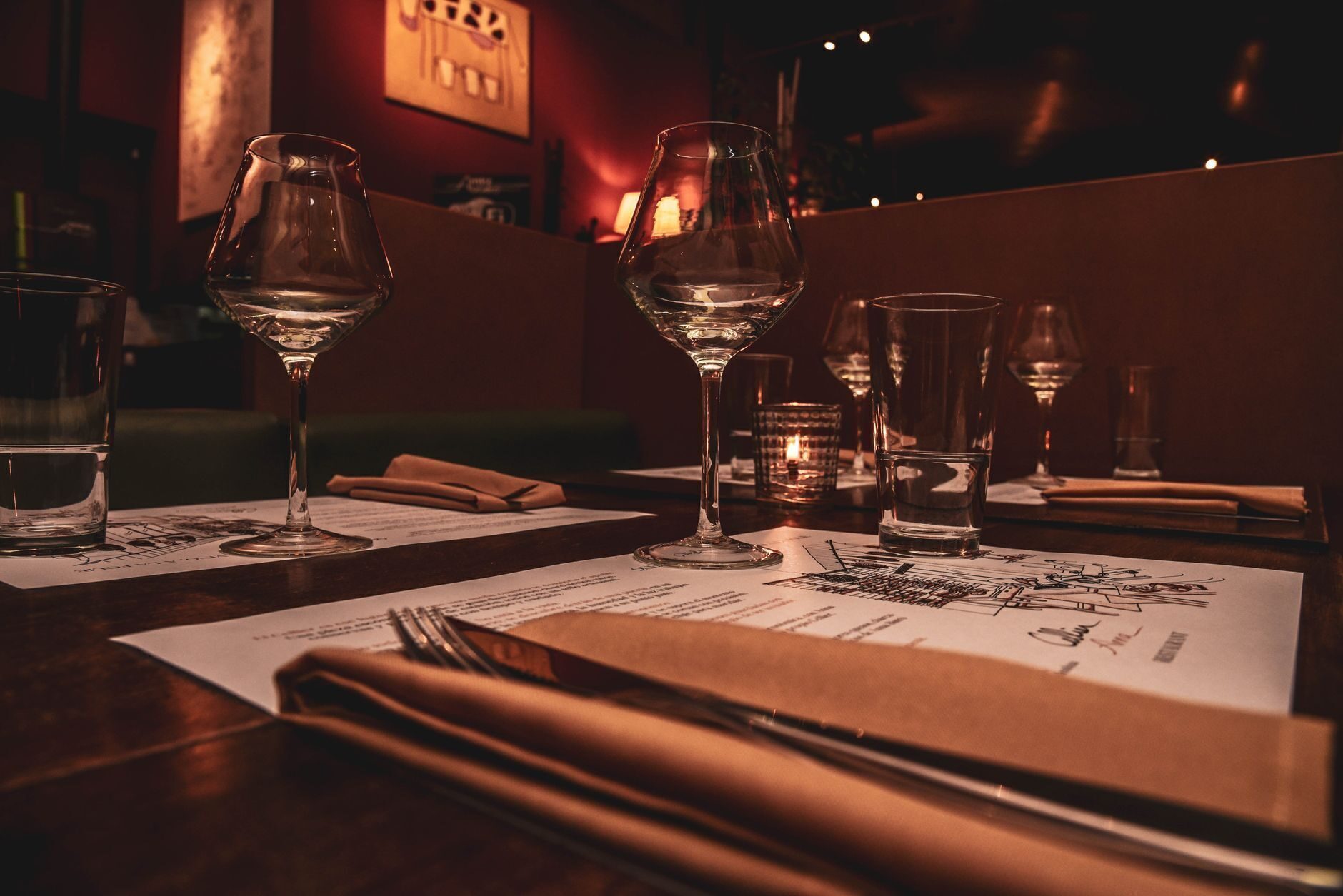 An empty restaurant table laid with wine glasses, flatware, folded napkins and a tea candle, shot from seat height
