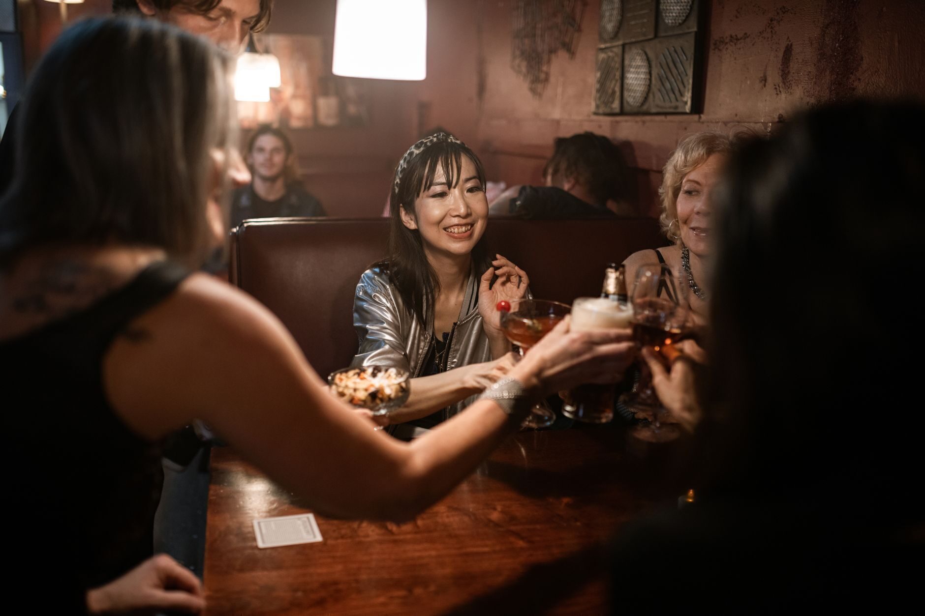 A group leaning in together at a dark leather booth under a warm amber pendant